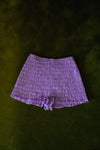 Purple smocked cotton bloomers worn with a lilac striped cardigan, showing the short silhouette and ruffled edges.